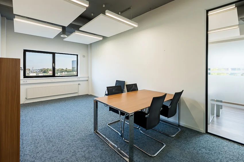 Moderne vergaderruimte aan de K.P. van der Mandelelaan met een houten tafel, vier stoelen en uitzicht op de stad.